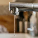 Grifo de cocina moderno con poca presión de agua soltando un hilo fino, ilustrando problemas de suministro en el hogar.